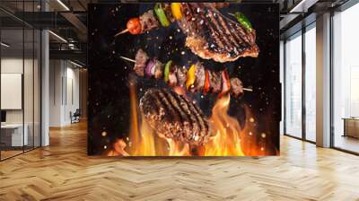 Tasty beef steaks and skewers flying above cast iron grate with fire flames. Freeze motion barbecue concept. Wall mural