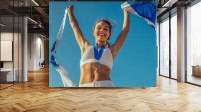 Athletic youngster cheering and clutching French flag after competition. A smiling, fit, athletic woman celebrating her Olympic gold medal. Raising national flag Wall mural