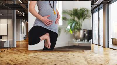 Young woman in early pregnancy doing tree pose holding belly Wall mural