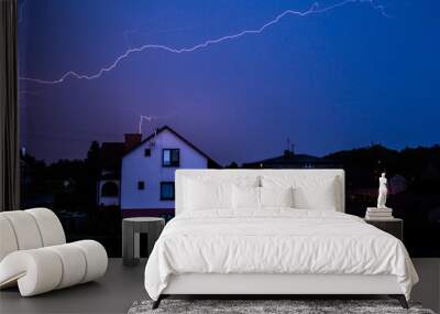 Long lightning from the storm glowing on the sky above rural houses at evening Wall mural