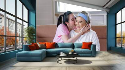 Asian young woman take care and  support with kiss, that make feel good and smile older mother in living room. family concept Wall mural