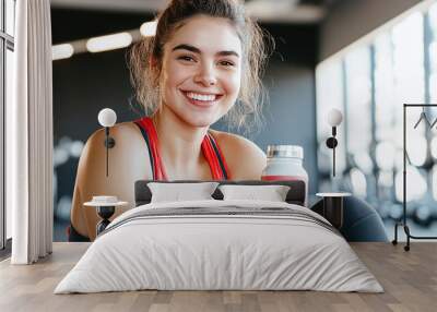 a smiling young fit woman holding a protein shake or water bottle at the gym Wall mural