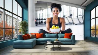 a young fit woman holding a bowl of fresh fruits at the gym, healthy lifestyle and diet, meal plan Wall mural