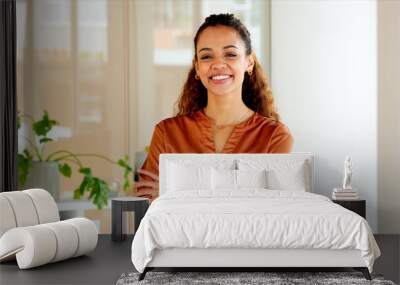 Confident stylish woman laughing with arms crossed and standing inside a modern office near a window. Face portrait of a happy hispanic female entrepreneur looking cheerful about successful business Wall mural