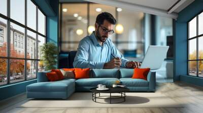 Busy young latin businessman working in office using laptop checking documents. Serious professional businessman hr manager a accounting report doing project overview. Copy space, Generative AI Wall mural