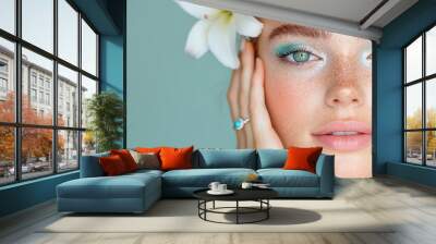 Portrait of a woman with turquoise eyeshadow and a white lily against a light teal background. Soft and fresh beauty concept for spring and summer promotions, banners, and cosmetic advertising with co Wall mural