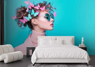 Stylish woman with pink butterfly headpiece and sunglasses, wearing pastel pink blazer, standing against bright blue background, bold fashion concept, creative and chic, space for text.

 Wall mural