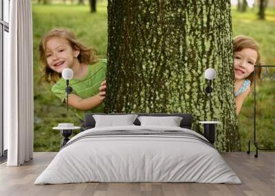 Two twin little girls playing in tree trunk Wall mural