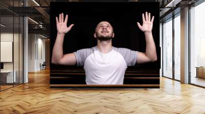 A Christian man in white shirt is sitting with his hands up and praying with humble heart in the church Wall mural