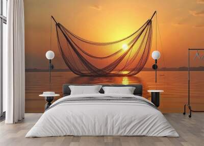 A large fishing net silhouetted against an orange and yellow sunset sky, reflected in the calm waters of a lake or ocean Wall mural