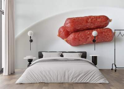 Three red delicious salami sausages on a white plate Wall mural