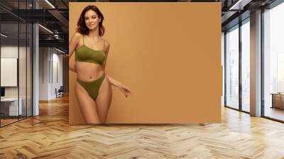 Adorable beautiful caucasian woman with slim fit figure in olive color inner wear posing on yellow studio background. Concept of female body, health, sport, spa, ad Wall mural