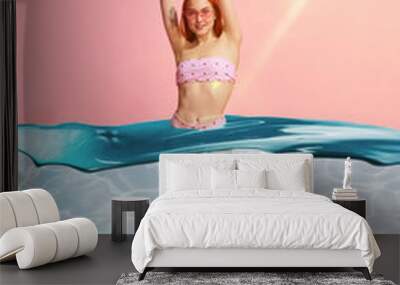 Beautiful redhead woman with fit, slim body in stylish, comfortable swimsuit against pink studio background with water design Wall mural