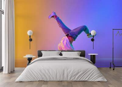 Creative young guy in casual clothes dancing hip-hop contemporary, breakdance against gradient studio background in neon light Wall mural