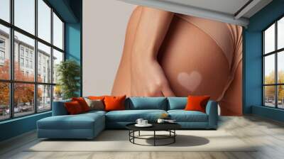 Cropped image with slim female body with tanned skin and paint heart liquid tan spray with airbrush on buttocks over white studio background Wall mural