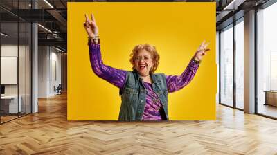 Elderly woman making peace sign and laughing dressed denim jacket and vibrant purple top. Happy expression. Concept of empowerment of older adults, active seniors in modern life, fashion and style. Wall mural