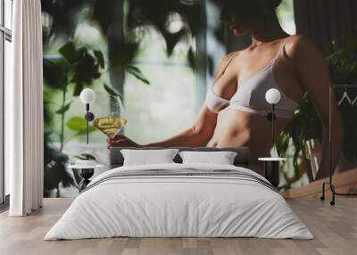 Fit, young woman in white lingerie holding glass of white wine, leaned on wooden table surrounded by lush greenery and natural light. Concept of alcoholic drink, relax, summer, holidays, vacation. Ad Wall mural