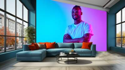 Full length african man smiling and looking at camera crosed hands over colorful studio background in neon. Wall mural