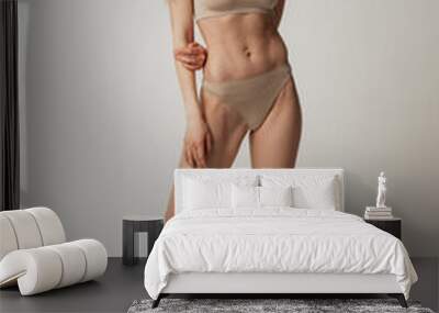 Full-length portrait of beautiful young woman with sportive muscular body posing in beige cotton underwear isolated over grey studio background Wall mural