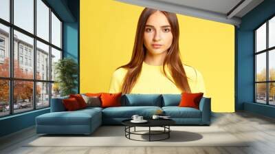 Portrait of beautiful young girl in stylish clothes looking at camera with calmness and confidence against sunny yellow studio background. Concept of business, beauty and fashion, sales season. Ad Wall mural