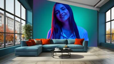 Portrait of joyful young girl looking at camera smiling cheerfully against gradient studio background in vibrant neon light. Concept of human emotions, business, beauty and fashion, sales season. Ad Wall mural