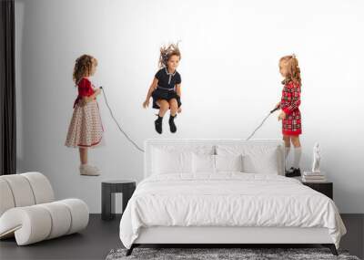 Portrait of little girls, children playing together, jumping over a rope isolated on white studio background Wall mural