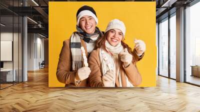 Portrait of stylish young man and woman, lovely couple in winter clothes posing with marshmallow isolated over yellow background Wall mural