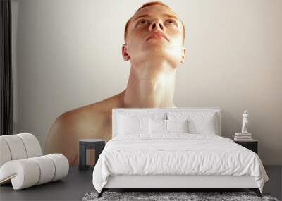 Portrait of young red-haired man posing shirtless, looking upwards isolated over grey studio background Wall mural