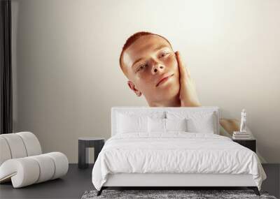 Portrait of young red-haired man with freckles touching cheeks, posing isolated over grey studio background. Shaving lotion Wall mural