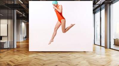 Portrait of young woman in swimming suit and cap jumping into water isolated over grey studio background Wall mural