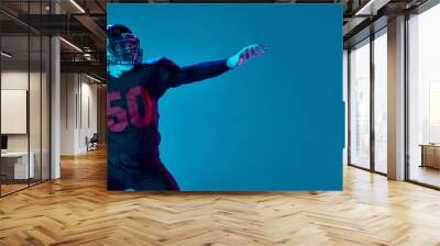 Strong throw. Professional american football player in sports team uniform and protective helmet isolated over blue background in neon light. Power, energy, achievements, skills Wall mural