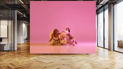 Two stylish female dancers in casual style clothes dancing contemporary choreography dance over crystal pink background. Concept of modern art, creativity, fusion Wall mural