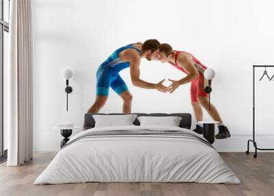 Young athlete man, wrestlers in blue and red uniform hand wrestling in neutral position on their feet against white studio background. Concept of sport, mixed martial arts, active lifestyle, movement. Wall mural