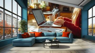 A woman typing on her laptop at a wooden kitchen table, with papers and a steaming cup of coffee beside her, soft sunlight illuminating the room, giving it a warm, Wall mural