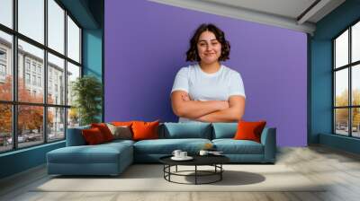 Curvy young woman smiling with crossed arms looking at camera, isolated on purple background. Copy space Wall mural