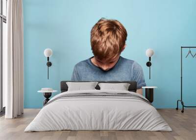 Unhappy caucasian young boy looking down, isolated on blue background. Copy space Wall mural