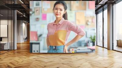 Young woman in pink shirt and blue jeans stands with a confused expression in an office setting. Wall mural