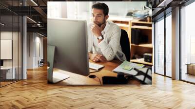 Hes never missed a deadline. Shot of a handsome young businessman working late on a computer in an office. Wall mural