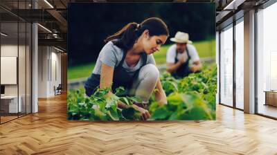 Nothing grows a garden like hard work. Shot of a young woman working in a garden with her husband in the background. Wall mural