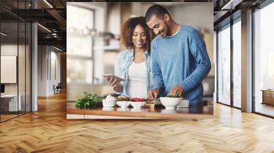 Young, happy and romantic couple cooking healthy food together following recipes online on a tablet. Smiling husband and wife making dinner or lunch in the kitchen at home Wall mural