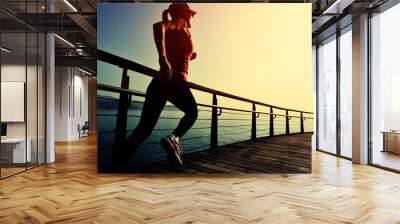 young fitness woman running on sunrise seaside boardwalk Wall mural