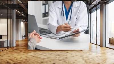 An elderly Asian doctor is talking to a younger Asian woman across a desk in a medical office, monthly health check appointment. Wall mural