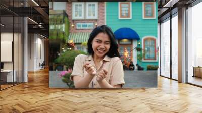 cheerful young asian woman holding sparkler to celebrate new year eve with garden party standing over colorful vintage house yard Wall mural