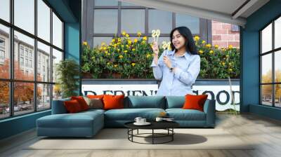 happy young woman asian hipster smiling to camera with raising hand holding 2024 number candle to celebrate new year eve, stylish female coworker standing in vintage house garden, outdoor Wall mural