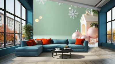 Festive holiday decorations featuring pink ornaments, snowflakes, and a white decorative house on a soft green background Wall mural