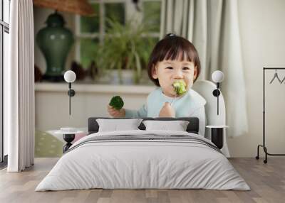 toddler girl eating  healthy  vegetable sitting on high chair beside a dinner table at home Wall mural