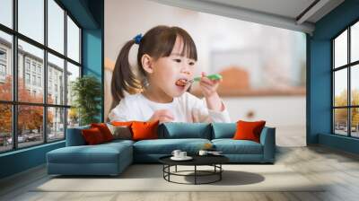 young girl eating fresh green vegetables  against real kitchen background Wall mural