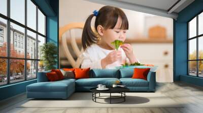 young girl eating fresh green vegetale against real kitchen background Wall mural