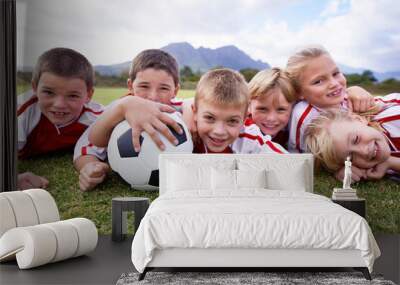 Children, soccer ball and relax on green grass or field for outdoor match, game. or team sports. Group of kids, friends or football players smile lying together for competition on stadium in nature Wall mural