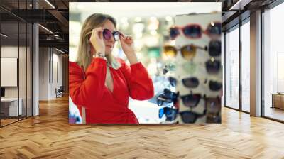 A woman in a red dress tries on glasses in a store. Wall mural